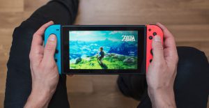 Gothenburg, Sweden - March 10, 2017: A shot from above of a young man's hands holding a neon coloured Nintendo Switch video game system developed and released by Nintendo Co., Ltd. in 2017. The system is turned on and the game The Legend of Zelda, Breath of the Wild is showing on the display. Shot on a hardwood floor background in a home environment.